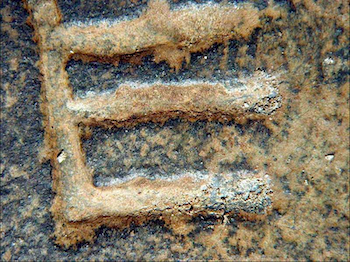 Figure 4. Note the biogenic pitting and black to brown patina formation within the letter "heh" [inverted] caused by black yeast-like fungi on the sandstone of the JI tablet. The patina layers consist of a lower biogenic iron oxide black to brown film above which is a light beige-ochre upper layer (the width of the engraved grooves of the letter is about 1 mm).